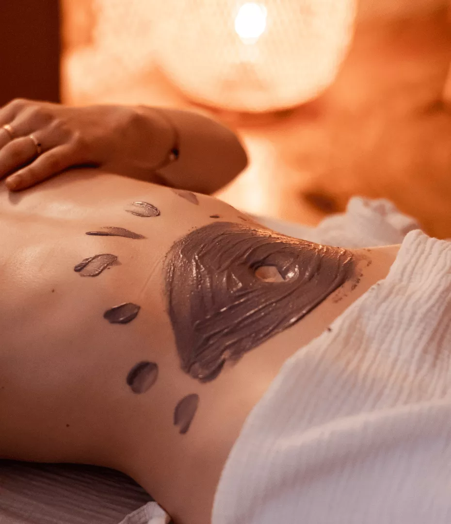 Un cataplasme de plantes et d'argiles en forme de soleil est posé sur le ventre d'une femme.