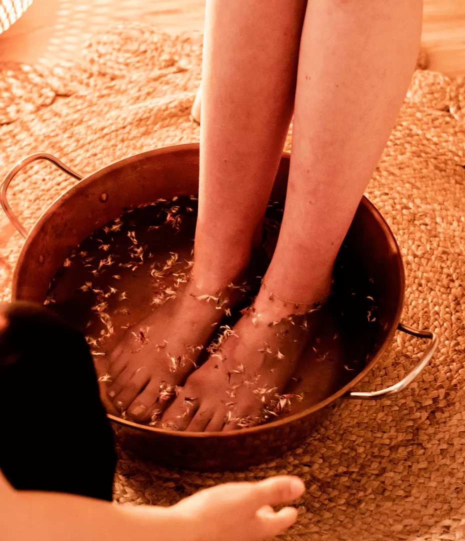 Une jeune femme prend un bain de pieds aux fleurs, dans une bassine en cuivre.