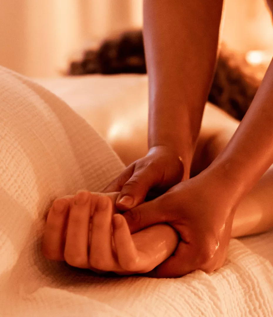 Massage de la main d'une cliente allongée sur le ventre. Les deux pouces de la masseuse sont au centre de la main.