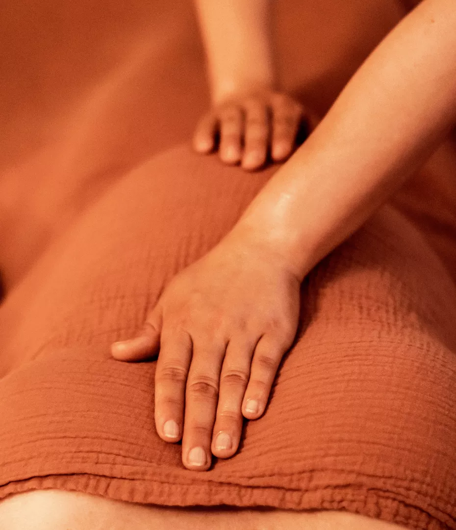 On voit une femme enceinte allongée sur le dos recouverte d'une couverture. La masseuse a posé une main sur son ventre et une main sur son coeur pour accompagner la respiration.