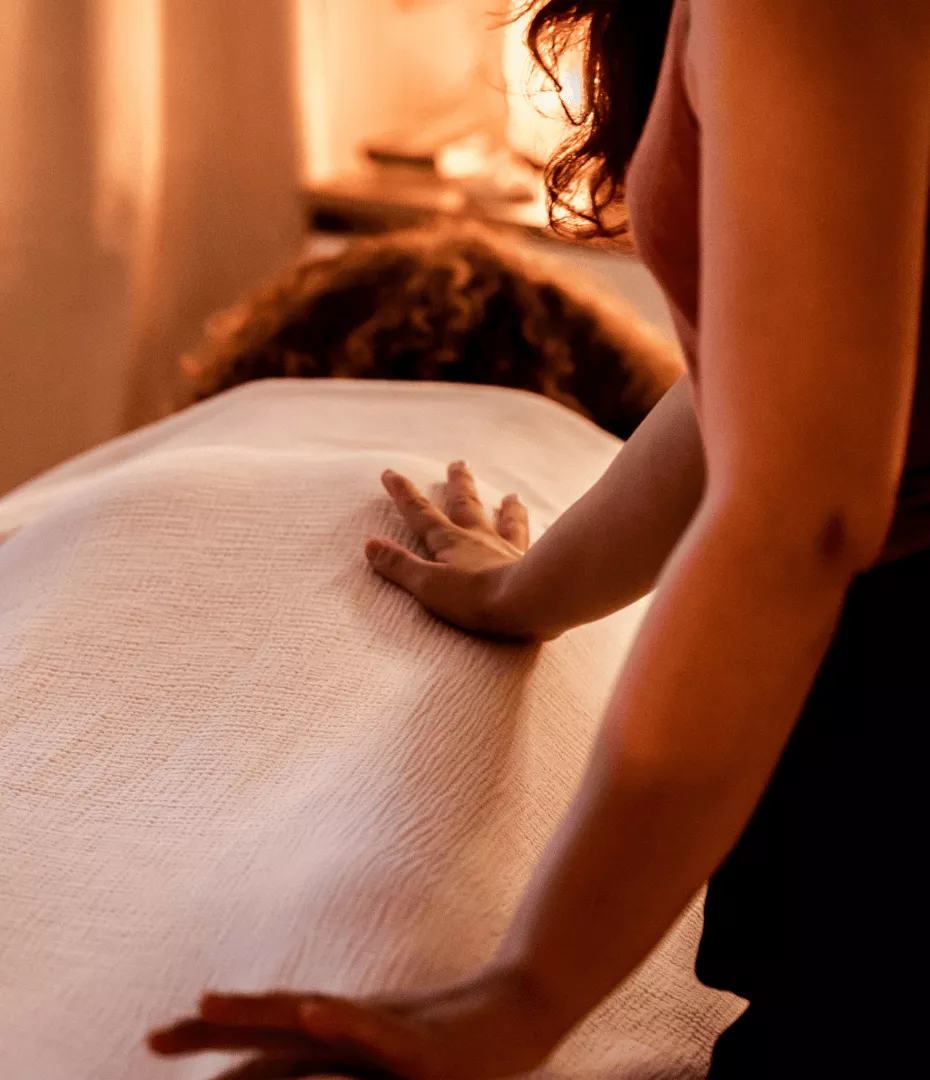 Une femme est allongée sur la table de massage, recouverte d'une couverture. La masseuse pose ces mains elle pour accompagner sa respiration.